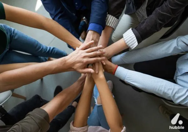 Diverse team members placing hands together in a show of unity and teamwork, symbolizing employee engagement and collaboration.