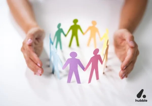 Hands gently encircling a circle of paper cut-out figures in various colours, symbolising diversity, inclusion, and unity in the workplace.